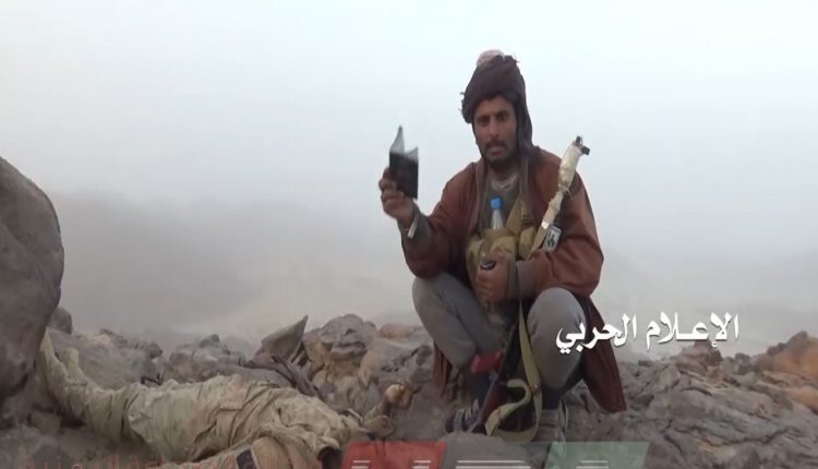 قتيل ثالث من قوات التحالف بجواره احد افراد الجيش اليمني يشاهد هوية القتيل في جبهة المهاشمة بمحافظة الجوف